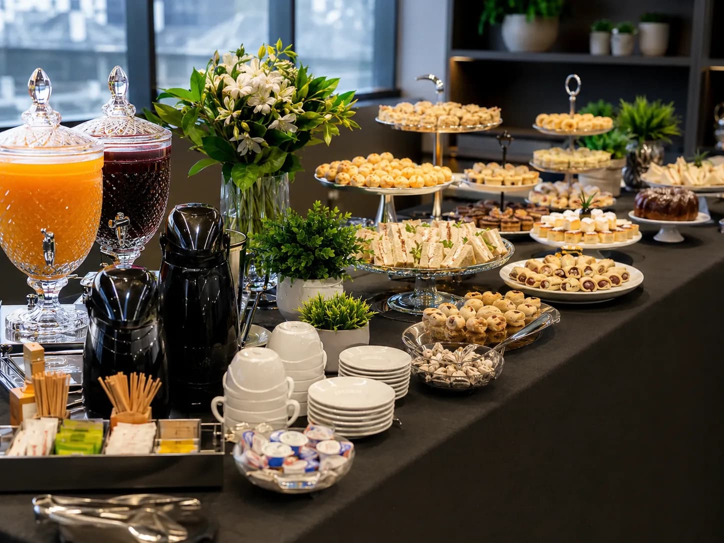 Mesa de coffee break corporativo com sucos, cafés, louças e finger foods em ambiente empresarial